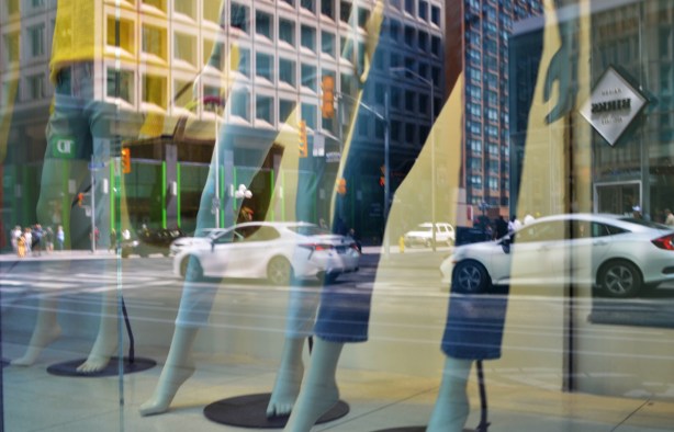 reflections in a store window, legs of mannequins in cut off jeans, white cars traffic on the street