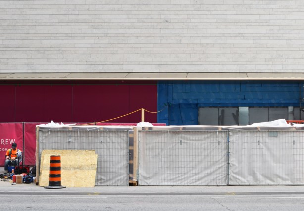a workman sits outside beside hoardings on Bloor street in front of Holt Renfrew