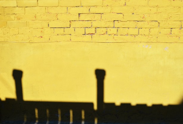 yellow wall with a black shadow of a fence along the bottom 
