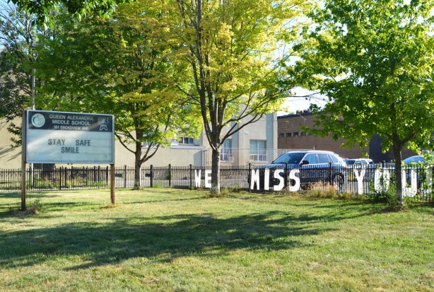 on the fence by a high school, words in white attached to the fence that say we miss you