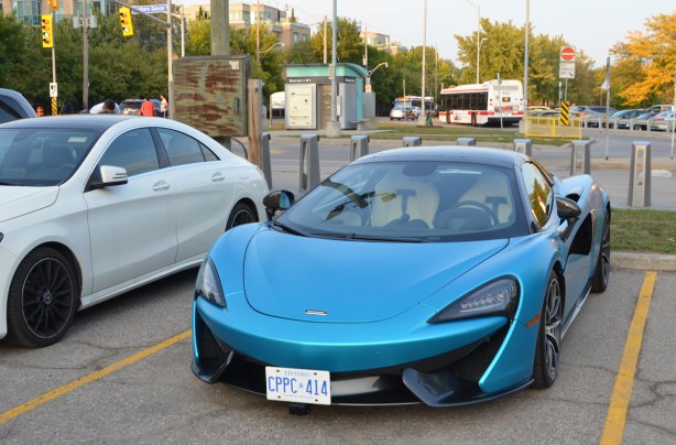 new blue Mclaren sports car parked ina parking lot at Woodbine beach, beside a white car and in front of a TTC bus stop