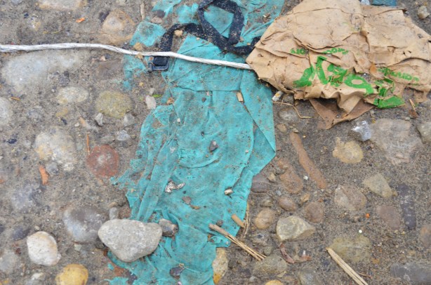 a blue belt, a length of rope and a brown Sobeys bag, trash on the ground along with a an old and torn turquoise shirt, dirt and rocks on the ground