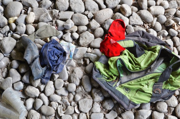 trash on the rocks, a green and black backpack, a red sock, and a rolled up blue article of clothing