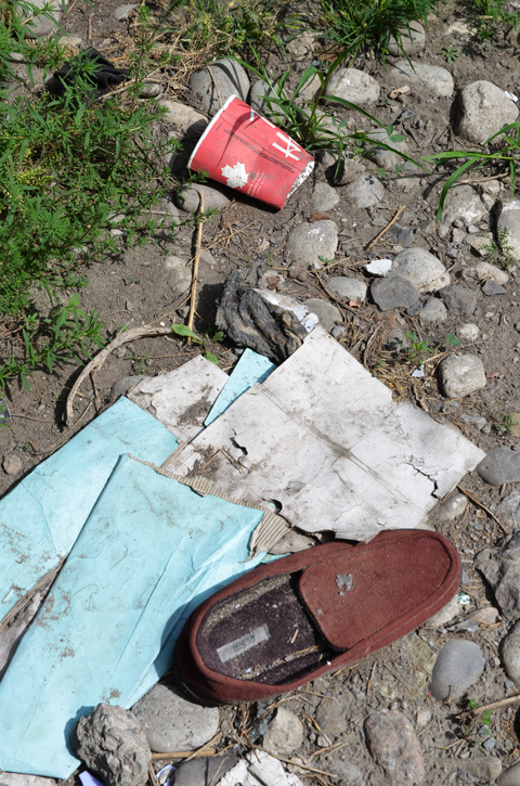 an old brown slipper, some turquoise and white paper, and an empty and squashed red Tims coffee cup, all rubbish lying on the ground 