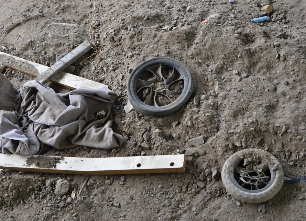 2 small wheels, not the same, and some pieces of wood, in the dirt, 