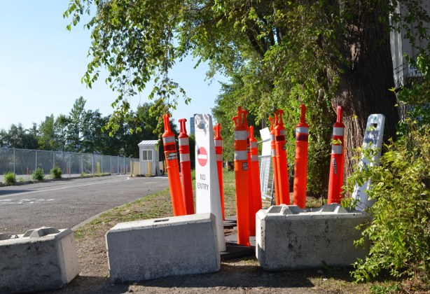 a collection of orange bollards for traffic, sitting beside the road and driveway leading to a parking lot. Parking lot booth in the background, empty 