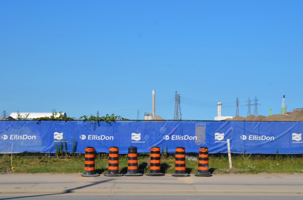 blue vinyl on hoardings around a construction site with six large orange and black traffic cones in front