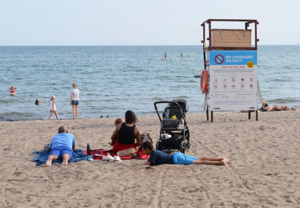 a family sits together on the beach, the youngest is a baby in mother's lap. stroller is beside them, empty lifeguard station too 