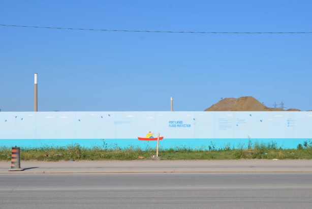 large painting on hoardings of a blue stripe on the bottom representing water of Lake Ontario and a small red boat