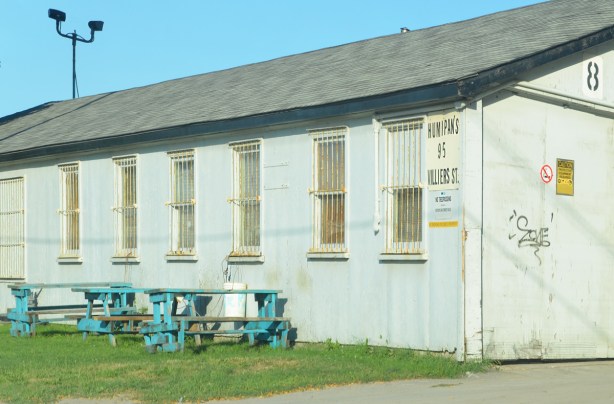 old building, one storey, with rusty metal bars on the windows, turquoise picnic tables outside, 
