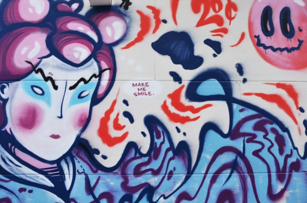 words, make me smile, and a Japanese looking face on a mural in an alley 