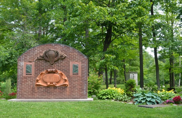 a brick wall with details from Royal Conservatory of Music building, music hall carving, and two bas-relief bronzes of men, Sir Ernest McMilland Dr. Healey Willan