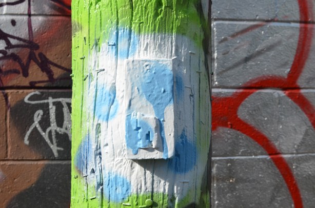 old stikman on a wood pole, only legs remaining, pole has been freshly covered with white and light blue spray paint 