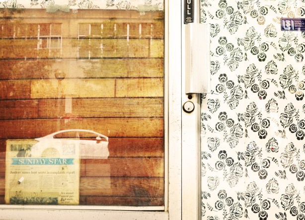 boarded over window beside a door covered with wallpaper. Sunday Star newspaper stuck between the boards and the glass of the window 