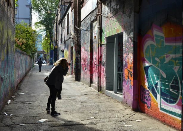 a woman takes a picture of street art in Graffiti Alley, late afternoon with low sun and long shadows 