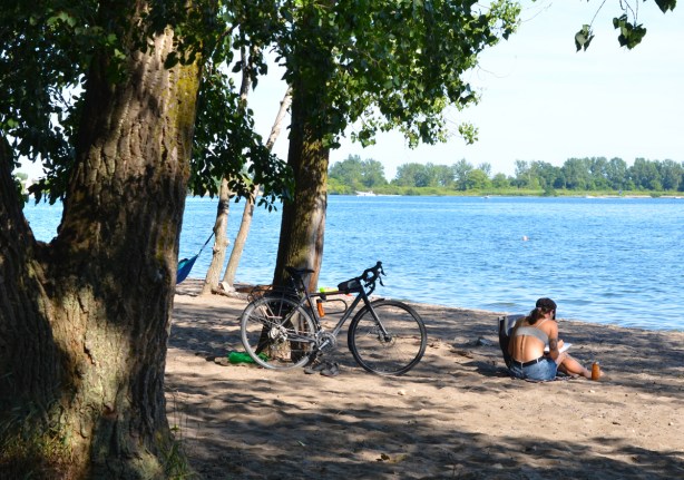 a woman sits on the sand at Cherry Beach, under a tree, with bike parked against the tree