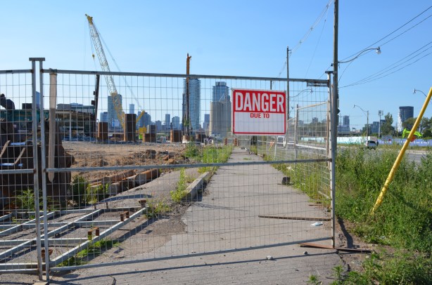 danger due to sign on a metal fence surrounding construction site which includes the sidewalk, Toronto skyline in the distance 