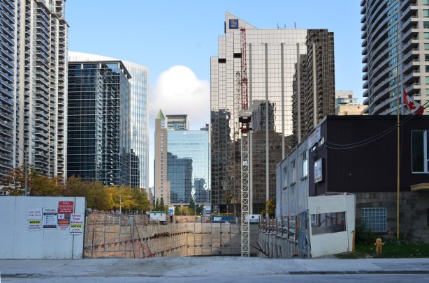 a large hole in the ground, construction at Yonge and Spring Garden, old Legion building in the right, tall North York buildings in the background 
