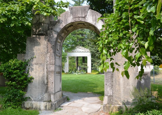 a statue under an arch as seen from an arch farther away, greenery, garden