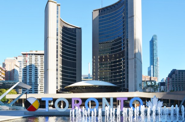 Nathan Phillips square in Toronto with fountains going in the reflecting pool, 3 D sign, and two towers of new city hall 