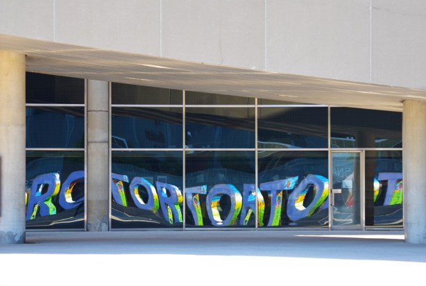 the Toronto sign reflected in the lower window of city hall 