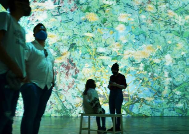 vincent Van Gogh Immersive Exhibit, 4 people, turquoise flowers, 2 men standing, one person sitting on a bench 