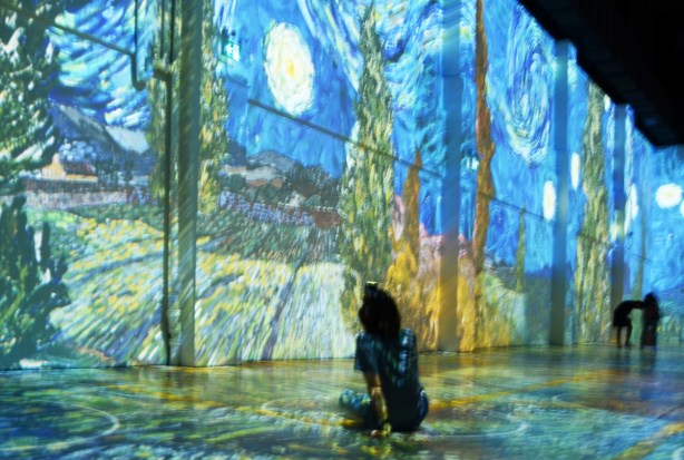 Vincent Van Gogh Immersive exhibit - person sitting on floor, taking aphoto with camera, starry starry night