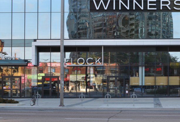 reflections in the window of Winners store at Yonge and Shephard, shows low rise older brick storefronts on the other (west) sideof Yonge 