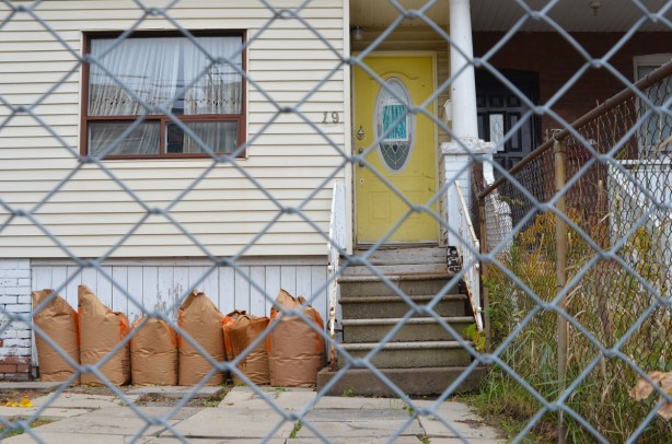 through a chainlink gate, front yard is square concrete patio stones, yellow front door 