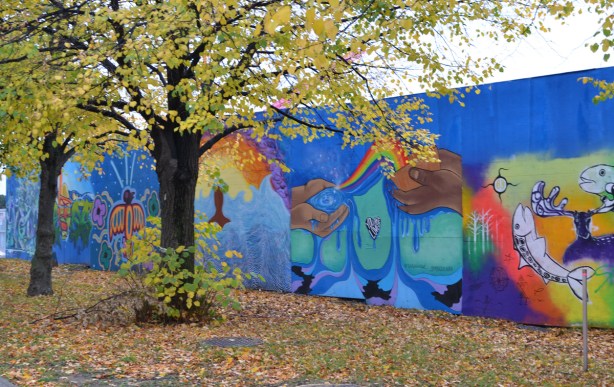 autumn trees in front of hoardings covered with murals, wallnoize, leaves on the ground, 