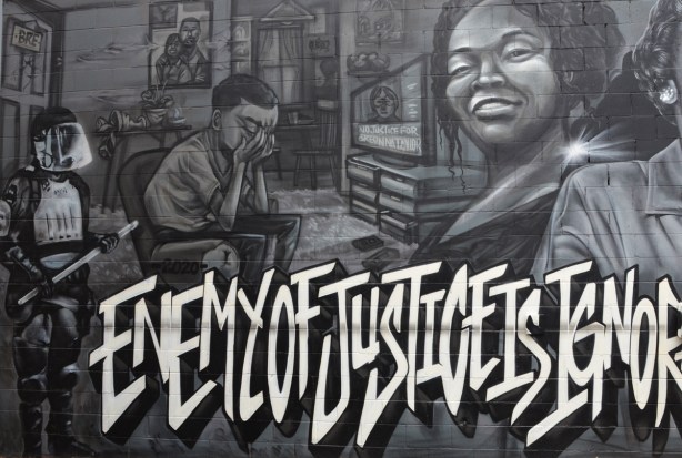 part of the Enemy of Justice mural, policeman standing by door, man sitting with hands over his eyes as TV is broadcasting about Breonna Taylor murder by policemen 