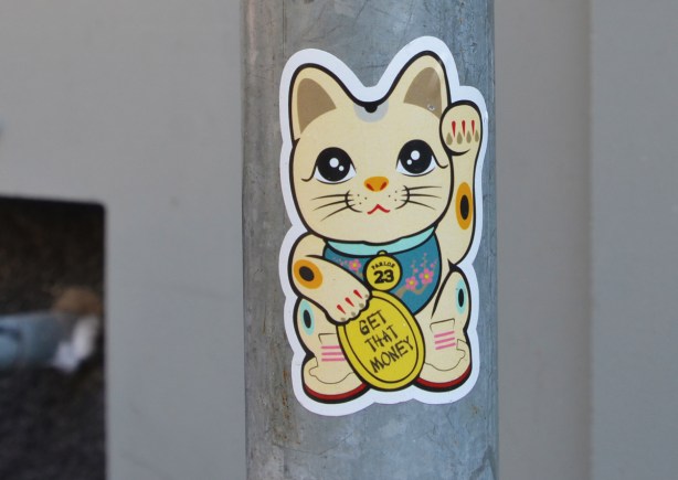 happy cat waving sticker, holding gold coin that says get the money 