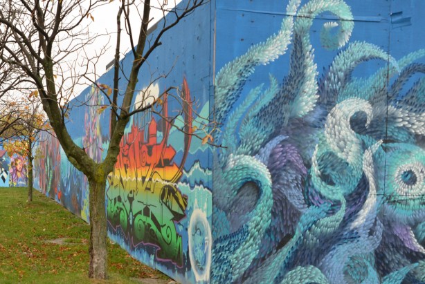 looking along a wall of murals on blue hoardings
