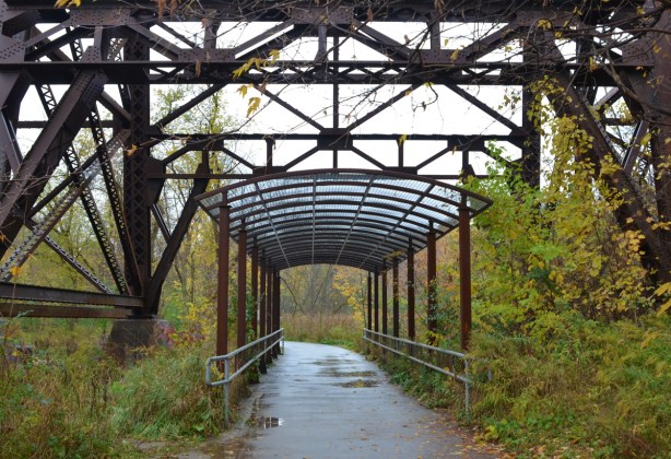 a metal canopy over a path and under a metal railway bridge 