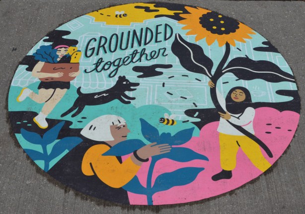 a painting on the sidewalk, a circle with words grounded together, pictures of women with plants and flowers, a dog chasing a bird. 