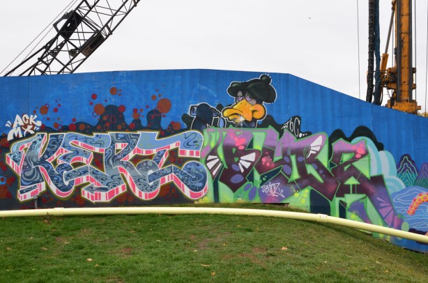 a duck character looks over the top of two text based graffiti murals one says kerz and the other is by bubzart