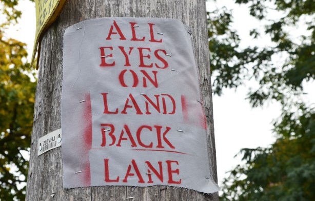 on a wood utility pole, a poster made of fabric that says All Eyes on Land back Lane 