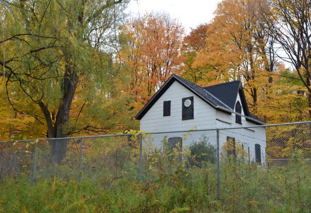 old white house, built 1878, now in park, with metal fence around it because of renovations, autumn, with trees in golds and oranges 