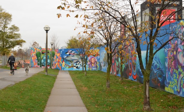 looking along a wall of murals on blue hoardings to where they cross and block the sidewalk