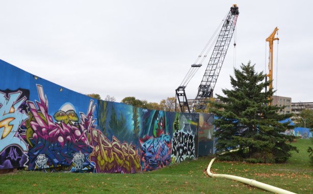pine tree beside hoardings around a construction site that have been painted by wallnoize, a group of street artists who have each painted a mural on a section of the wall 