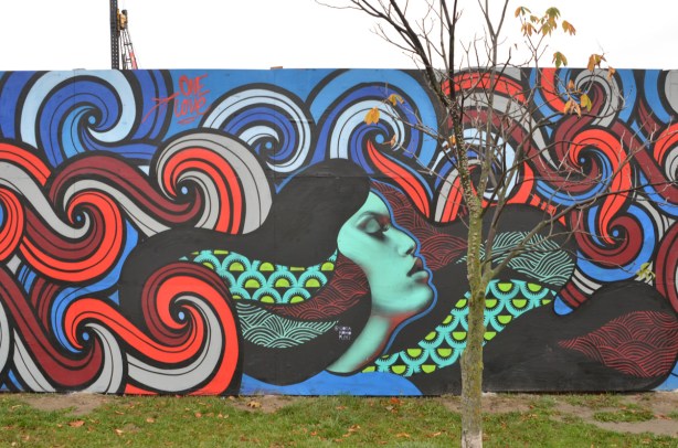 wallnoize street art murals on blue hoardings around new water treatment plant, a woman with long flowing hair and with her eyes closed