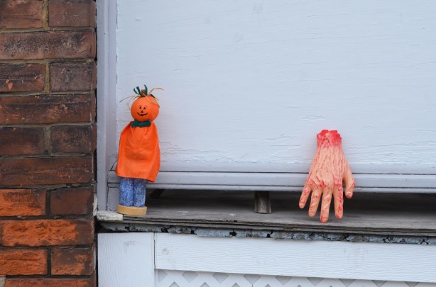 an an exterior window sill, a bloody h and, not real, and a small figure with a pumpkin for a head, armless, wearing an orange top