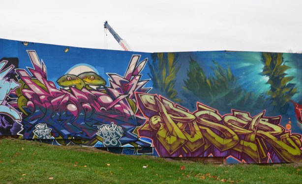 two text murals on hoardings, on the right is poser, and on the left is one with two eel heads poking up on top