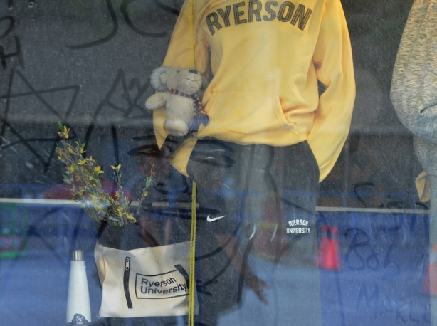 in the window of the Ryerson bookstore, mannequin wearing yellow Ryerson sweatshirt, dirty window, someone has drawn the picture of a man's face in the dirt 