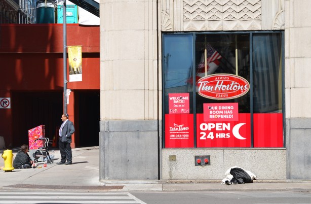 a Jewish man stands outside a TIm Hortons talking to a woman who is sitting on the sidewalk pan handling. downtown Toronto
