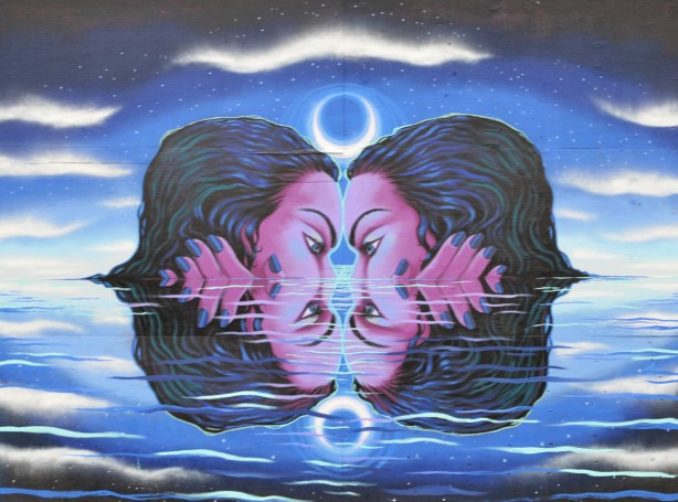 mural by Julii McMillan of two identical heads nose to nose in the water up to their noses, reflections of the two. hands beside heads so they reflect too. water, dark, moonlight 