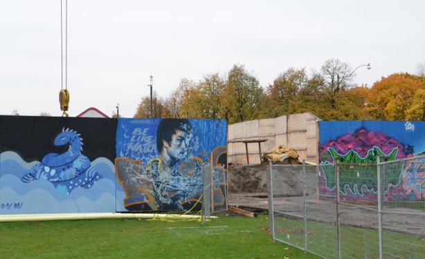 wallnoize street art murals on blue hoardings around new water treatment plant, by an entrance to the site, a mural of a man