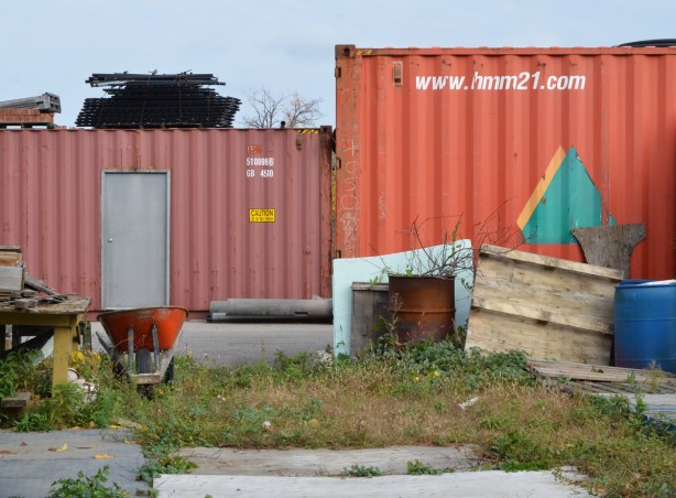 two shipping containers and some other junk used in a lot with a garden