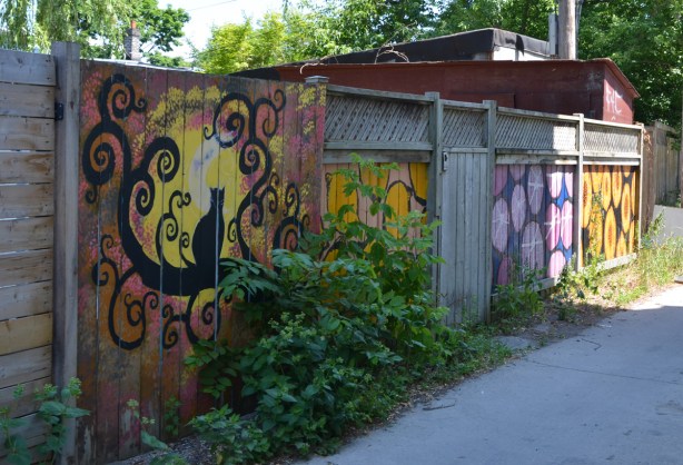 mural on a fence in an alley, a black sitting on a tree branch with curly branches, moonlight behind the cat 
