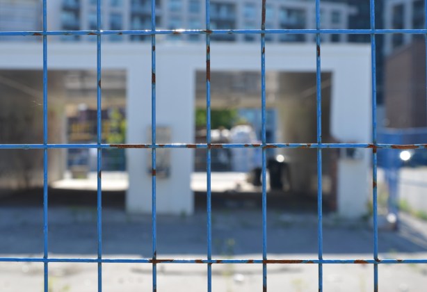 blue metal constructioon fence in the foreground with out of focus building behind, an old abandoned car wash